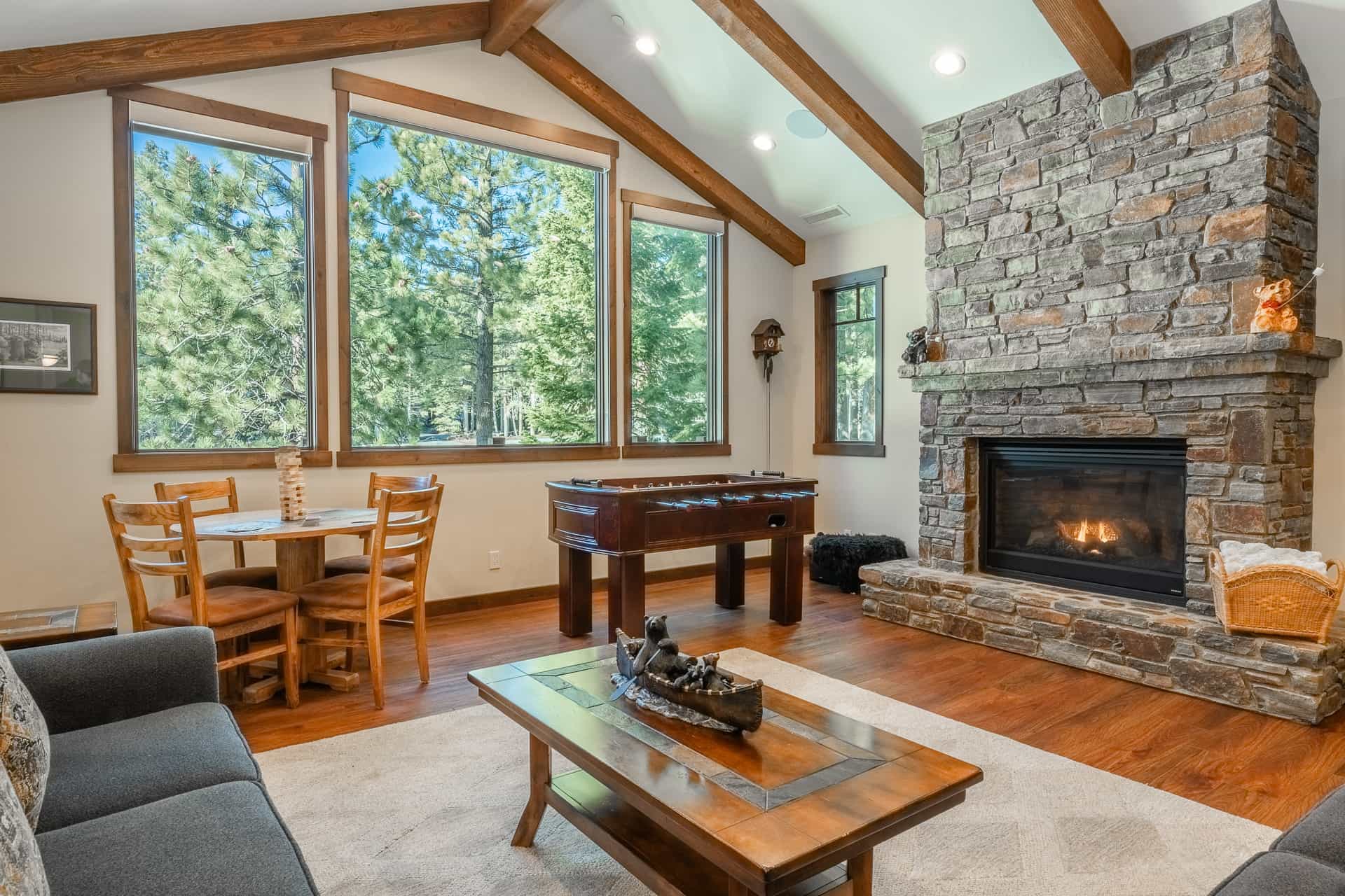 Spacious living room with a stone fireplace and large windows with forest views